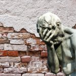 statue covering face in front of old broken brick wall