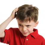 Child in red shirt scratching head while looking confused